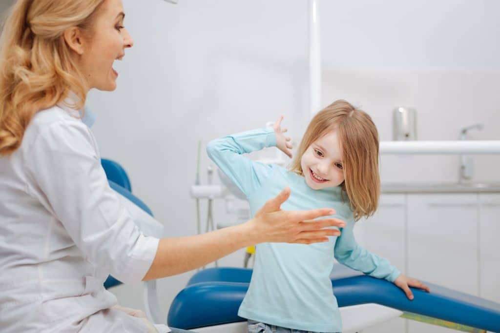 Let us be friends now. Emotional cute prominent dentist giving a high five to her little patient after extracting her tooth