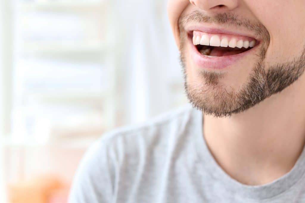 Young man with beautiful smile on white background. Teeth whitening