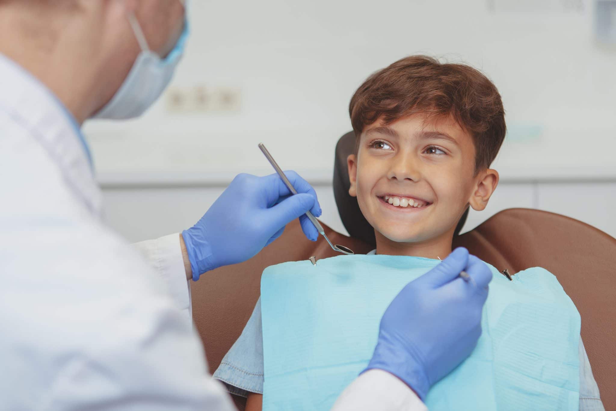 Adorable happy healthy boy smiling cheerfully at his dentist, sitting in a dental chair. Cropped shot of a professional dentist checking teeth of a lovely boy